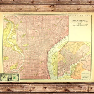 May include: Vintage map of Philadelphia, featuring a detailed street grid and surrounding areas. The map is in shades of red, yellow, and beige, with text that reads "Philadelphia" and "Rand McNally Indexed Atlas." A one-dollar bill is placed at the bottom.