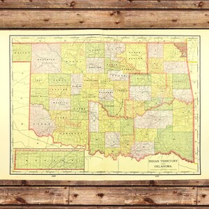 May include: A vintage map of the Indian Territory and Oklahoma, featuring a detailed layout of counties in shades of green, yellow, and red. The map is printed on aged paper and is set against a wooden background.