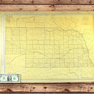 May include: An antique map of Nebraska from the Commercial Atlas of America, with detailed county lines and geographical features. The map is in shades of yellow and brown, with text in black. A one-dollar bill is placed at the bottom left corner.