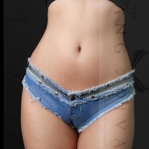 May include: Light blue denim shorts with a frayed hem and a decorative silver-tone studded belt. The shorts have a low-rise waist and a classic five-pocket design. The shorts are made of a light wash denim.