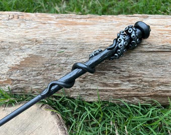 May include: A black wand with a detailed octopus design at the top. The wand is made of a dark, textured material and has a smooth, polished finish.