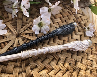 May include: Two decorative wands with a white and black feathered design. The wands have a crystal ball at the end. The wands are on a woven basket background.