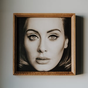 May include: A framed black and white photograph of a woman with dark hair and intense eyes. The photo is in a simple wooden frame.