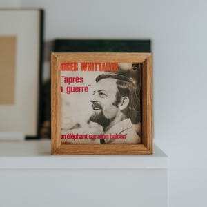 May include: A framed vintage record album cover featuring a black and white photo of a man with a beard. The album title is "après la guerre" and the artist is "Roger Whittaker".
