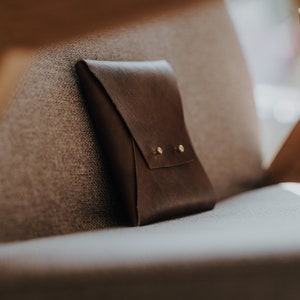 May include: A brown leather pouch with two brass rivets on a grey fabric surface.
