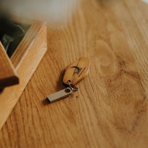 May include: Wooden USB flash drive with a keychain attached, engraved with a crescent moon and text. The flash drive rests on a wooden surface next to an open wooden box. The text on the flash drive reads "ROUTE DU MOULIN".