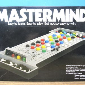 May include: A Mastermind board game box featuring a black background with white text that reads Mastermind, Easy to learn. Easy to play. But not so easy to win. The box displays a gray plastic game board with colorful red, blue, yellow, green, white, and black pegs.