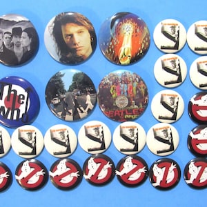 May include: A collection of round buttons featuring various designs. Some buttons display band members, album art, and logos, including The Who, Led Zeppelin, and Ghostbusters. The buttons are in various colors, including black, white, red, and blue.