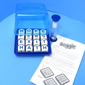 May include: A blue Boggle word game set. The game includes a blue plastic grid with lettered dice, a timer, and instructions. The dice show the letters: H, O, P, E, P, E, W, S, E, X, I, T, H, A, T. The game is on a blue surface.