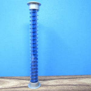 May include: A tall, cylindrical, clear plastic storage tube featuring a vibrant blue internal spiral insert. The container is capped with a light gray circular lid at the top and a matching light gray circular base at the bottom, standing upright.