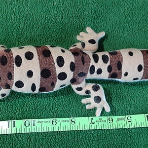 May include: A brown and black plush gecko with a white belly, measuring 14 inches long. The gecko has a spotted pattern and brown stripes.