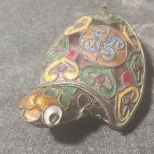 May include: A turtle-shaped brooch crafted from silver-toned metal with intricate filigree wirework. The shell and head are decorated with colorful enamel in shades of yellow, green, red, and blue, featuring swirling patterns and a central circular motif.