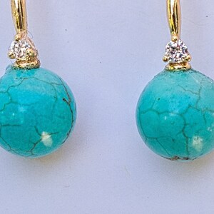 May include: A pair of turquoise and gold earrings with a small diamond accent on each earring.
