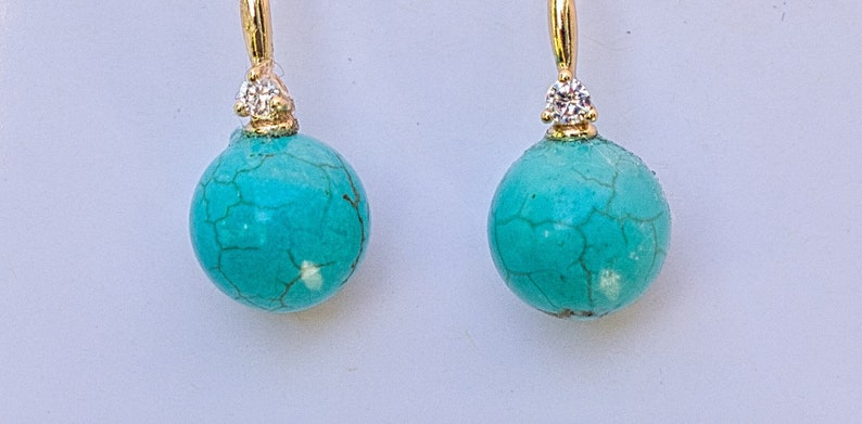 May include: A pair of turquoise and gold earrings with a small diamond accent on each earring.