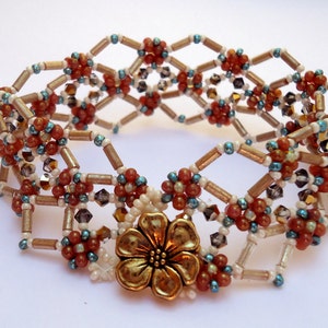 May include: A beaded bracelet with a gold flower charm. The bracelet is made with brown, white, and blue beads in a geometric pattern.