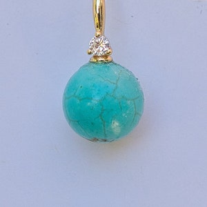 May include: A turquoise gemstone earring with a small diamond accent. The earring is made of gold and has a round shape.
