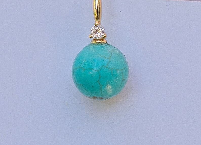 May include: A turquoise gemstone earring with a small diamond accent. The earring is made of gold and has a round shape.
