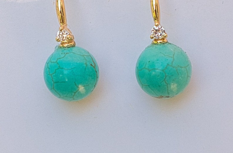 May include: A pair of turquoise and gold earrings with a small diamond accent on each earring.
