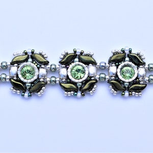 May include: A green and silver beaded bracelet with a repeating pattern of flower-like designs. Each design features a green gemstone in the center.
