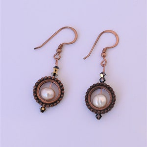 May include: Copper earrings with a pearl and crystal accents. The earrings feature a circular design with a pearl in the center and a crystal dangle.