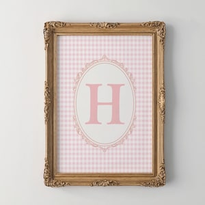 May include: A framed print with a pink and white gingham pattern and a pink letter "H" in a decorative oval frame.
