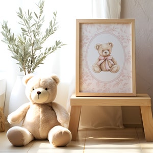 Pu&ograve; includere: Una stampa ad acquerello incorniciata di un orsacchiotto con un fiocco rosa, su uno sfondo floreale rosa. La stampa &egrave; esposta su uno sgabello di legno accanto a un orsacchiotto di peluche.