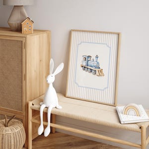 May include: A blue and white watercolor illustration of a toy train on a light blue background with a white border. The train is on a white and blue striped background with a wooden frame.