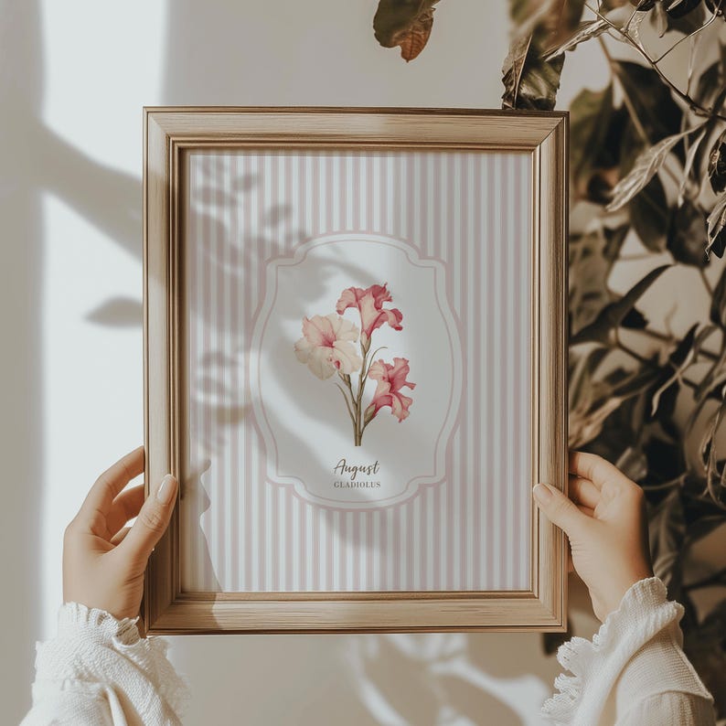 May include: A framed print with a pink and white striped background. The print features a watercolor illustration of pink and white gladiolus flowers with the text "August Gladiolus".