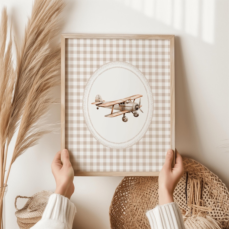 Pu&ograve; includere: Una stampa incorniciata con un'illustrazione ad acquerello di un aereo d'epoca. L'opera d'arte &egrave; ambientata su un motivo a quadri vichy beige e bianco, incorniciata in legno chiaro. L'aereo &egrave; marrone e argento, con un'elica.