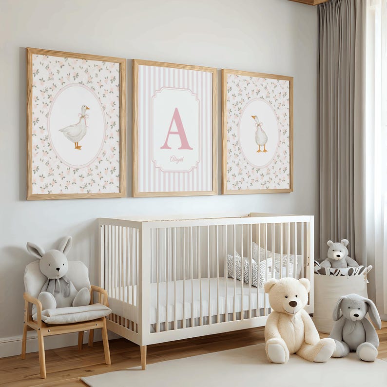 May include: Three framed wall art prints featuring a white goose illustration in two oval frames and a central frame with the letter A and the name Abigail, displayed above a white wooden crib with plush animal toys on the floor and chair.