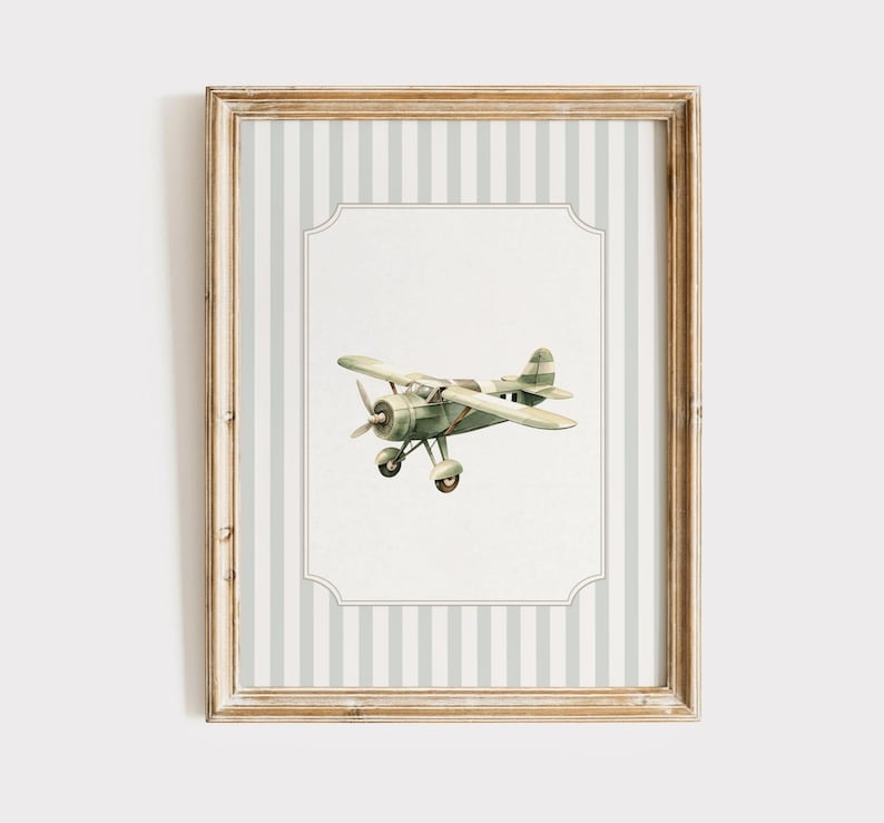 May include: A framed print featuring a vintage-style airplane illustration. The airplane is painted in shades of green and tan, set against a white background with a decorative border. The frame has a light wood finish and a striped background.