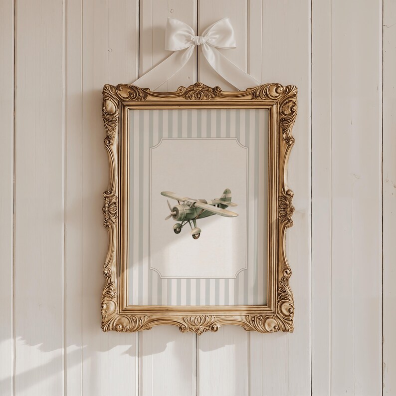 May include: A framed print featuring a vintage-style airplane. The print is set within a gold ornate frame and is suspended by a white bow. The background of the print has a striped pattern in light blue and white.