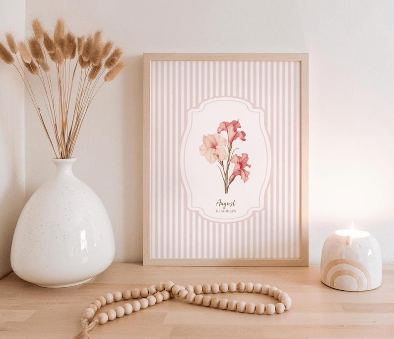 May include: A framed print with a pink and white striped background. The print features a watercolor illustration of pink and white gladiolus flowers with the text "August Gladiolus".