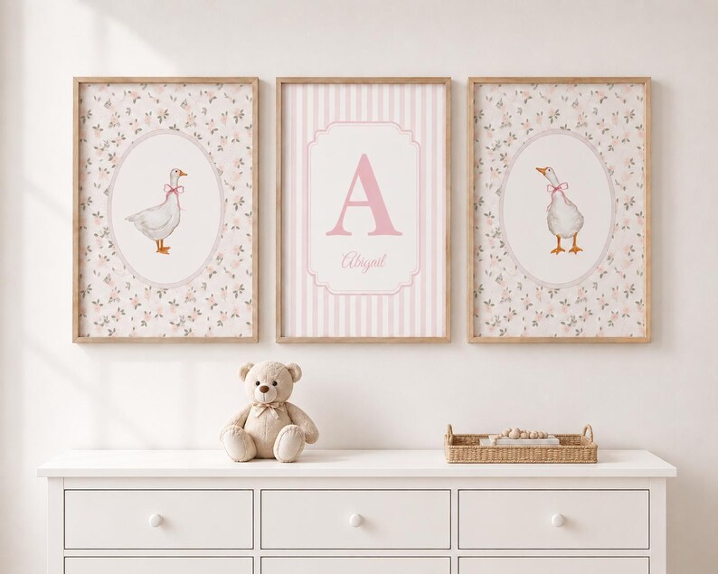 May include: Three framed wall art prints featuring a light pink and white color palette. The two outer prints display a white goose with a pink bow inside an oval, while the center print features a large pink letter A and the name Abigail.