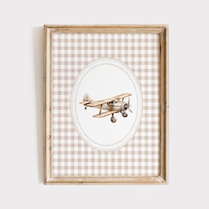 Pu&ograve; includere: Una stampa incorniciata con un'illustrazione ad acquerello di un biplano vintage. Il biplano &egrave; in tonalit&agrave; marroni e beige, su un ovale bianco con un bordo a forma di corda. Lo sfondo &egrave; un motivo a quadretti beige e bianco.