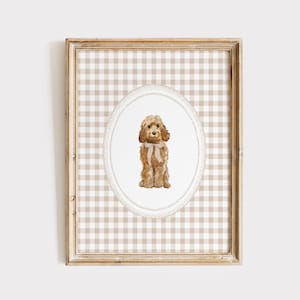 Può includere: Una stampa ad acquerello incorniciata con un cane marrone seduto con un fiocco color crema. Il cane è centrato all'interno di una cornice ovale, su uno sfondo a scacchi beige e bianco. La cornice è di colore legno chiaro.