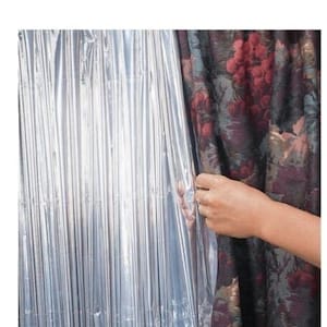 May include: A silver reflective curtain being pulled back to reveal a patterned curtain with red, green, and black floral designs.