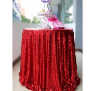 May include: A red round sequin tablecloth on a table. The tablecloth has a ruffled edge.