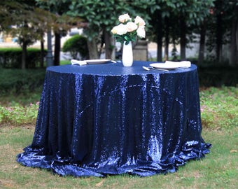 May include: A navy blue round table cover with a sequin texture. The table cover is draped over a round table and has a slight ruffle around the edge.