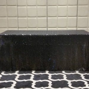 May include: A black sequined tablecloth draped over a table. The tablecloth is made of a shiny, sparkly fabric.