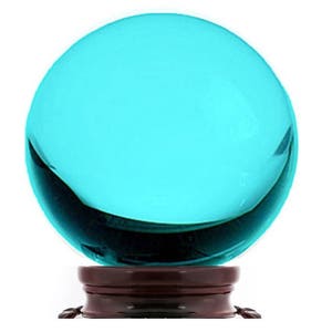 Può includere: Una sfera di vetro turchese su una base di legno marrone scuro. La sfera è liscia e riflettente.