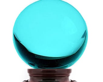 Puede incluir: Una esfera de vidrio turquesa sobre una base de madera marrón oscuro. La esfera es lisa y reflectante.