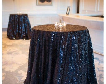 May include: Two round tables covered in dark blue sequin tablecloths. The tablecloths have a subtle shimmer and are draped over the tables.