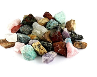 May include: A pile of assorted raw gemstones in colours including red, pink, green, blue, brown, and purple. The stones vary in size and shape, with diverse textures and patterns. The gemstones are arranged against a white backdrop.