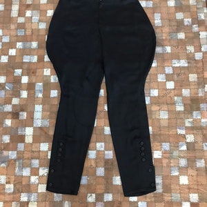 May include: Black riding pants with button detailing on the sides. The pants are made of a smooth, stretchy fabric.
