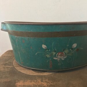 May include: A vintage teal blue metal tub with a gold trim and hand-painted floral design. The tub has a rounded shape and is perfect for a farmhouse or rustic decor.