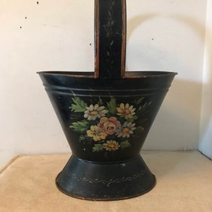 May include: A black metal basket with a painted floral design. The basket has a handle and a wide base. The flowers are painted in shades of pink, yellow, and white.