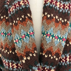 Puede incluir: Un c&aacute;rdigan de punto marr&oacute;n con un estampado geom&eacute;trico colorido. El c&aacute;rdigan tiene un cuello chal y est&aacute; hecho de un material suave y c&aacute;lido.