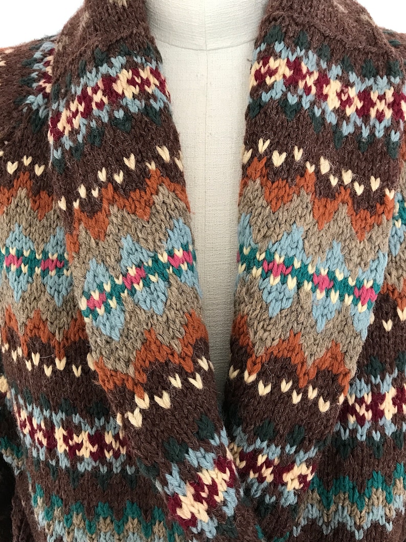 Puede incluir: Un c&aacute;rdigan de punto marr&oacute;n con un estampado geom&eacute;trico colorido. El c&aacute;rdigan tiene un cuello chal y est&aacute; hecho de un material suave y c&aacute;lido.