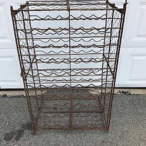 Puede incluir: Un gran estante para vino de metal oxidado con forma rectangular y múltiples filas de soportes de alambre curvos. El estante está diseñado para sostener botellas de vino.